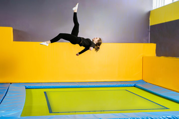 Young woman amateur acrobatic athlete jumping and exercising on a trampoline indoors, modern hobby...