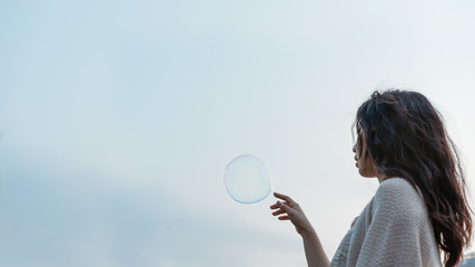 Long-haired girl in a backlight touching the bubble