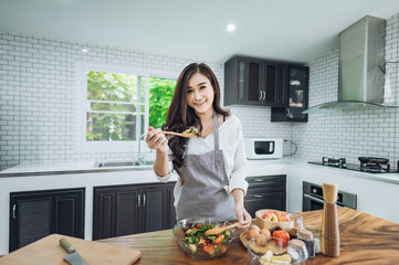 Image of young lady standing in kitchen using tablet computer and cooking vegetable salad with the tomatoes and avocado.