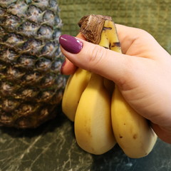 A bunch of bananas in a woman's hand against the background of a pineapple.