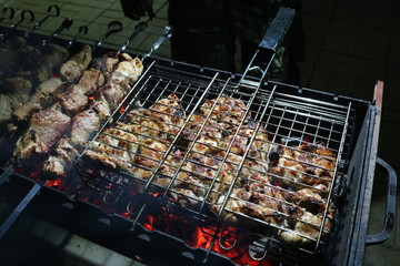 Grilled meat in an iron grill and skewers on skewers lying on the grill. Photographed in the evening street light. 