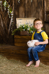 little boy in yellow T-shirt against background of wooden porch plays with white fluffy rabbit