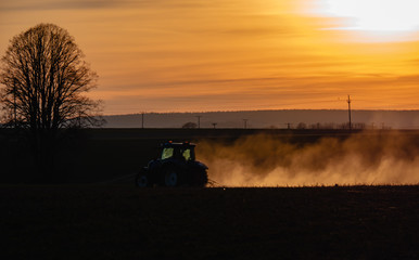 Fototapeta premium Tractor silhouette in the field on the orange-yellow sunset