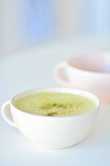 Homemade matcha latte on a white table, a light pink cup on the background, matcha green tea latte in a white cup with copy space. Matcha is a powder of green tea leaves and a delicious energy booster