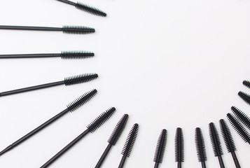 Black makeup brushes on top, eyelash and eyebrow combs on a white background with copy space lie around