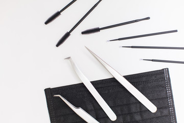 Black makeup brushes, eyelash and eyebrow combs on a white background, black mask for the safety of clients of a beauty salon with copy space