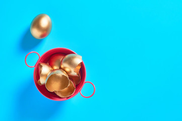 Red metal basin full of golden egg shells on blue background. Easter concept. Copy space. Top view