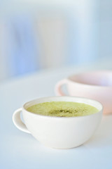 Homemade matcha latte on a white table, a light pink cup on the background, matcha green tea latte in a white cup with copy space. Matcha is a powder of green tea leaves and a delicious energy booster