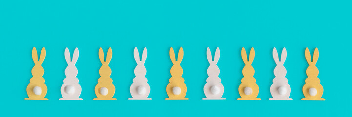 A row of decorative white and yellow Еaster bunnies isolated on a blue background. Happy Easter Holiday Minimal Concept. Creative flat lay. For design cards or web banners. Copy space