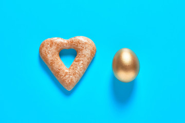 Gold egg and cookie in shape of heart on blue background. Easter concept. Top view