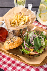 burger with cheese, red onion, French fries and lemonade on black wooden table