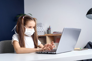 Distance learning online education. schoolgirl in medical mask studying at home, working at laptop notebook and doing school homework. coronavirus quarantine concept.