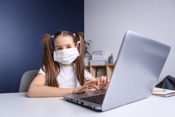 Distance learning online education. schoolgirl in medical mask studying at home, working at laptop notebook and doing school homework. covid quarantine concepte.