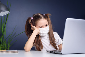 Distance learning online education. schoolgirl in medical mask studying at home, working at laptop notebook and doing school homework. coronavirus quarantine concepte.
