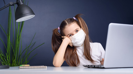 Distance learning online education. schoolgirl in medical mask studying at home, working at laptop notebook and doing school homework. coronavirus quarantine concepte.