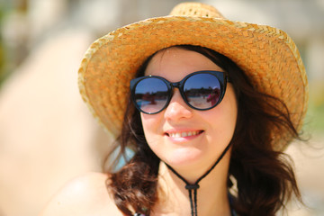 Portrait of a caucasian 35 year old woman wearing sunglasses and a straw hat and posing near the swimming pool 