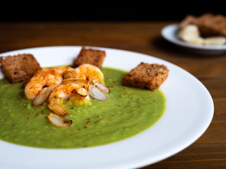 A plate of thick fresh green pea soup with prawns on a rustic wooden table with a garlic and croutons on the side. Close up.