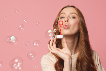 young female model blowing soap bubbles on pink background, close up shot