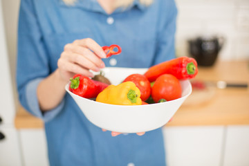 A girl in a blue denim shirt holds a white plate full of bell peppers