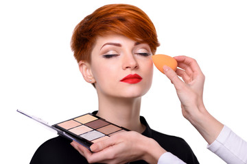 Makeup artist applying foundation on young woman's face using sponge. Beautiful young woman with...