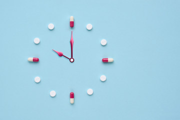 Clock created from pills and capsules on pastel blue background. Right time for using medicines....