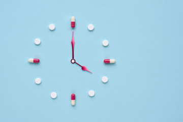 Clock created from pills and capsules on pastel blue background. Right time for using medicines. Flat lay.