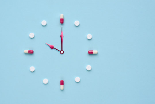 Clock created from pills and capsules on pastel blue background. Right time for using medicines. Flat lay.