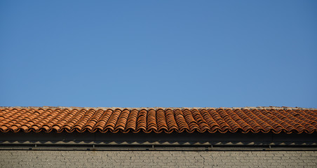 Terra Cotta roofing with ancient style built on top of a building.  Blue sky in background.