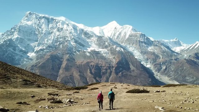 Couple trekking to Ice lake, part of the Annapurna Circuit Trek, Himalayas, Nepal. They are happy. Annapurna chain in the back, covered with snow. Clear weather, dry grass, snowy peaks. High altitude