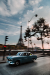Old car driving on the road with the Eiffel tower and the Seine river in the background.