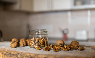 Walnut in a jar and scattered nuts which standing on a white vintage table with a kitchen on background. Walnuts is a healthy vegetarian protein nutritious food. Walnut on rustic old wood.