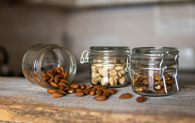 Almonds scattered on the white vintage table from a jar and with other nuts on background. Almond is a healthy vegetarian protein nutritious food. Almonds on rustic old wood.