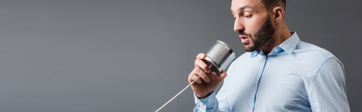 panoramic shot of bearded man taking while holding tin can isolated on grey