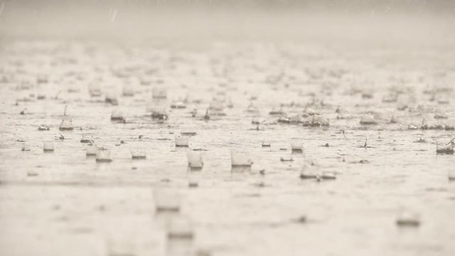Slow motion speed close up scene of dropping pattern when raining falling against water surface on cement floor, grain texture of raindrop in rainy season, flooding street after rain pour.