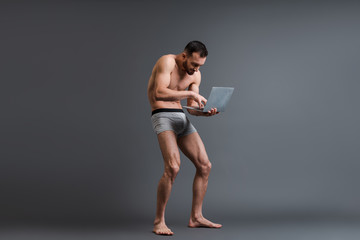 shirtless and stooped man in boxer shorts using laptop on grey