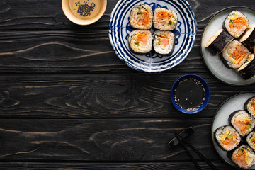 top view of sesame oil near plates with gimbap near chopsticks on wooden surface