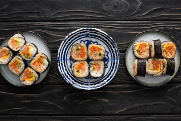 top view of plates with tasty and korean gimbap on wooden surface