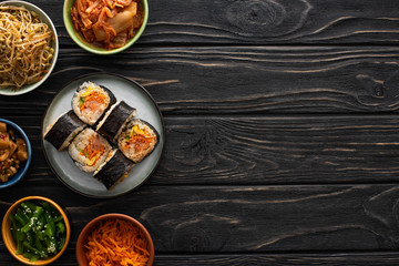 top view of plate with fresh gimbap near korean side dishes on wooden surface