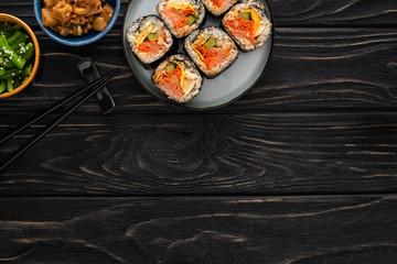 top view of chopsticks near plate with gimbap and korean side dishes on wooden surface