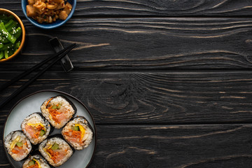 top view of chopsticks near plate with tasty gimbap and korean side dishes on wooden surface
