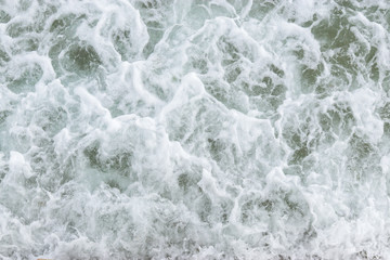 Fototapeta premium Top view texture waves, foaming and splashing in the ocean, sunny day. Beautiful tropical sea in summer season image by aerial view. Abstract sea background. Ocean waves close-up.