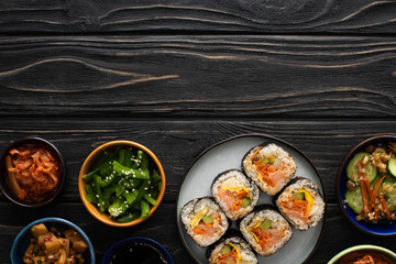 top view of plate with korean gimbap near side dishes on wooden surface