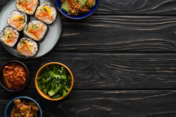 top view of korean side dishes near plate with rice rolls on wooden surface
