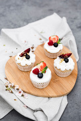 Vegan cupcakes with berries and coconut cream on a wooden board.