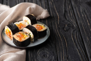 selective focus of tasty rice rolls with vegetables and salmon near cotton napkin on wooden surface