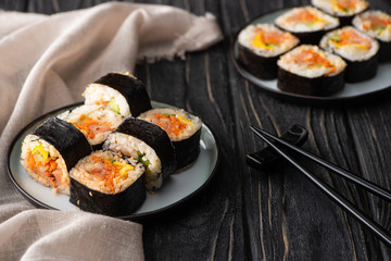 selective focus of tasty gimbap with vegetables and salmon on plates near chopsticks on wooden surface