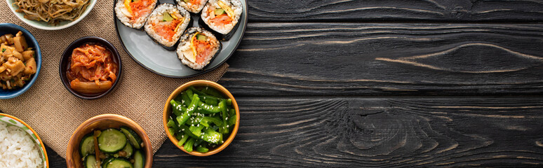 panoramic shot of tasty korean side dishes near rice rolls on wooden surface