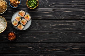 top view of bowls with korean side dishes near gimbap on wooden surface