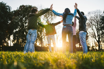 Group of young friends at park at sunset in circle with hands upwards - Teens in a moment of unity, fraternity, strength and team building