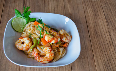 Noodles with shrimps and vegetables in a white plate on a dark wooden table.